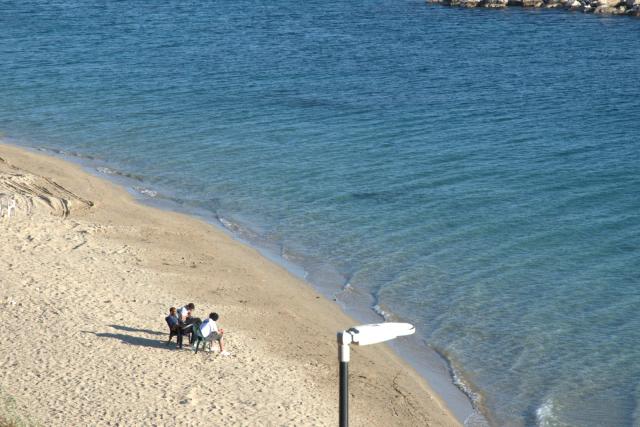 Una spiaggia di sabbia chiara vista dall'alto, con l'acqua del mare limpida e alcune persone sedute in riva