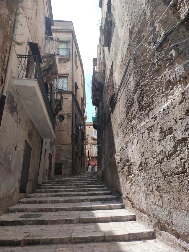 Una scalinata stretta fra le case alte della Città Vecchia di Taranto, con i gradini di pietra che salgono verso un vicolo