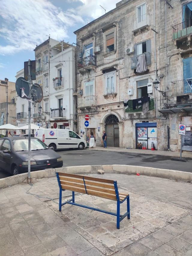 Via Garibaldi nella Città Vecchia di Taranto vista dal marciapiede sul mare, con una panchina in primo piano e i vecchi palazzi di pietra di fronte